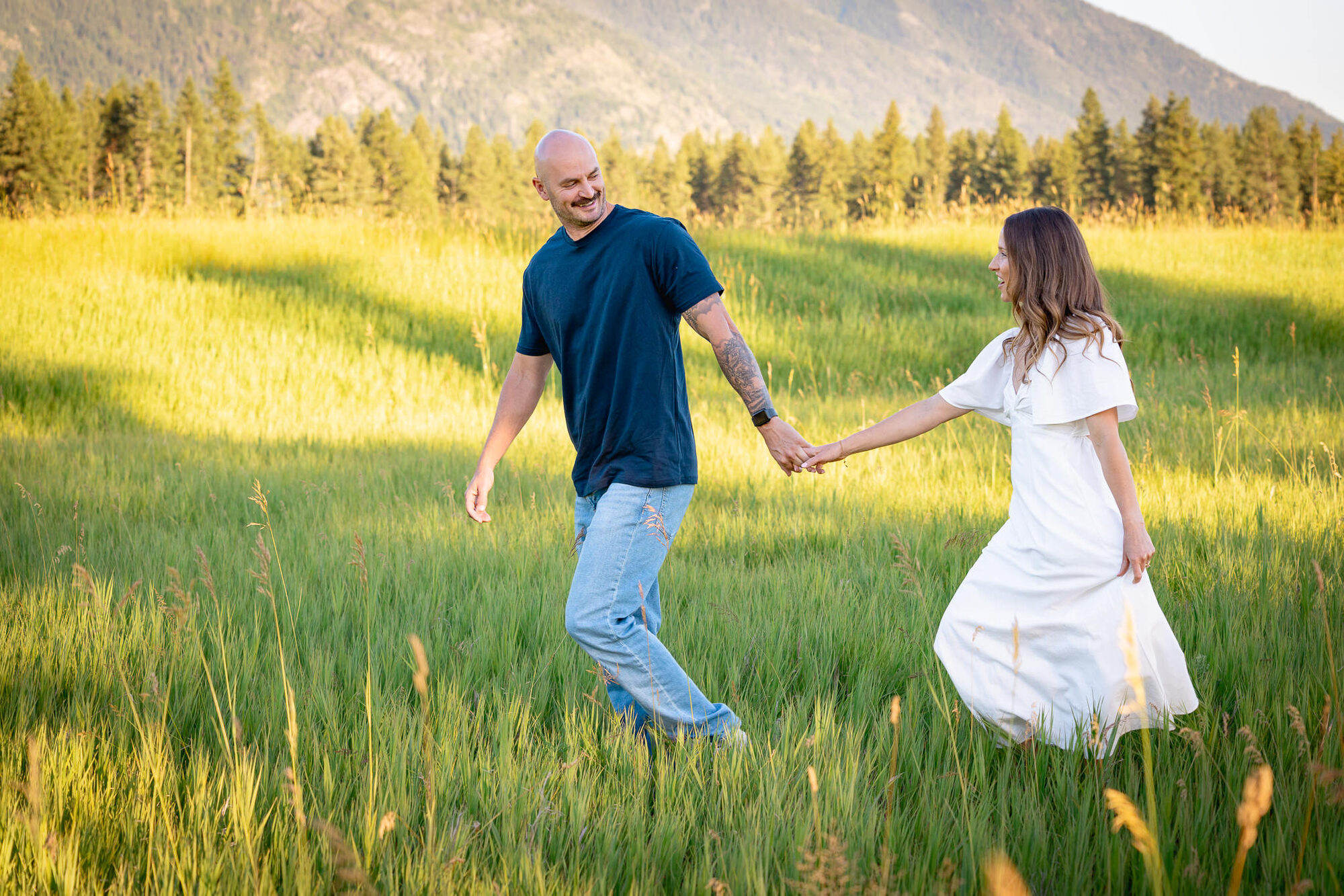 Couple walking hand in hand through a sunlit meadow, tall grass around them