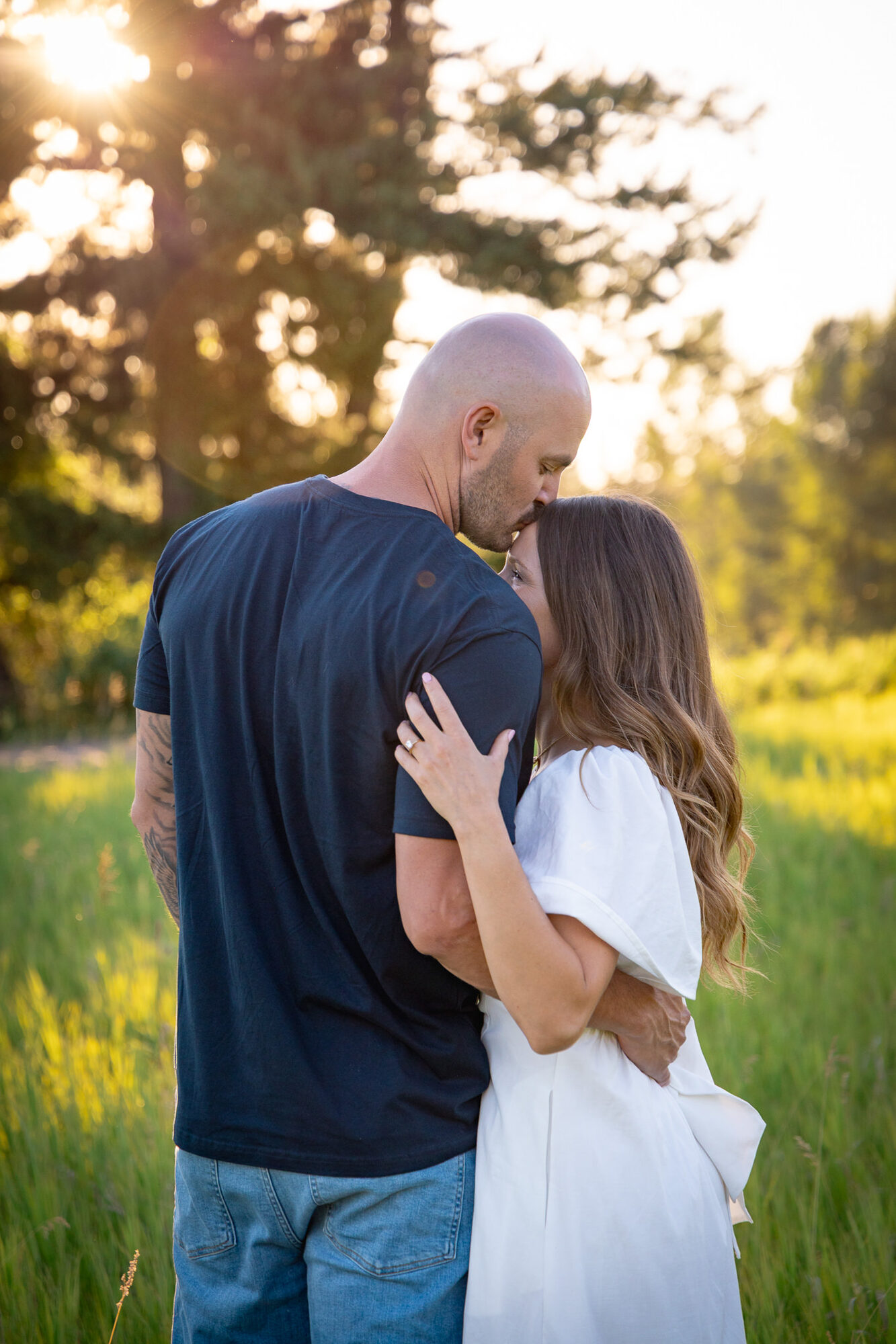 Couple walking through golden grass at sunset with pine trees in the background