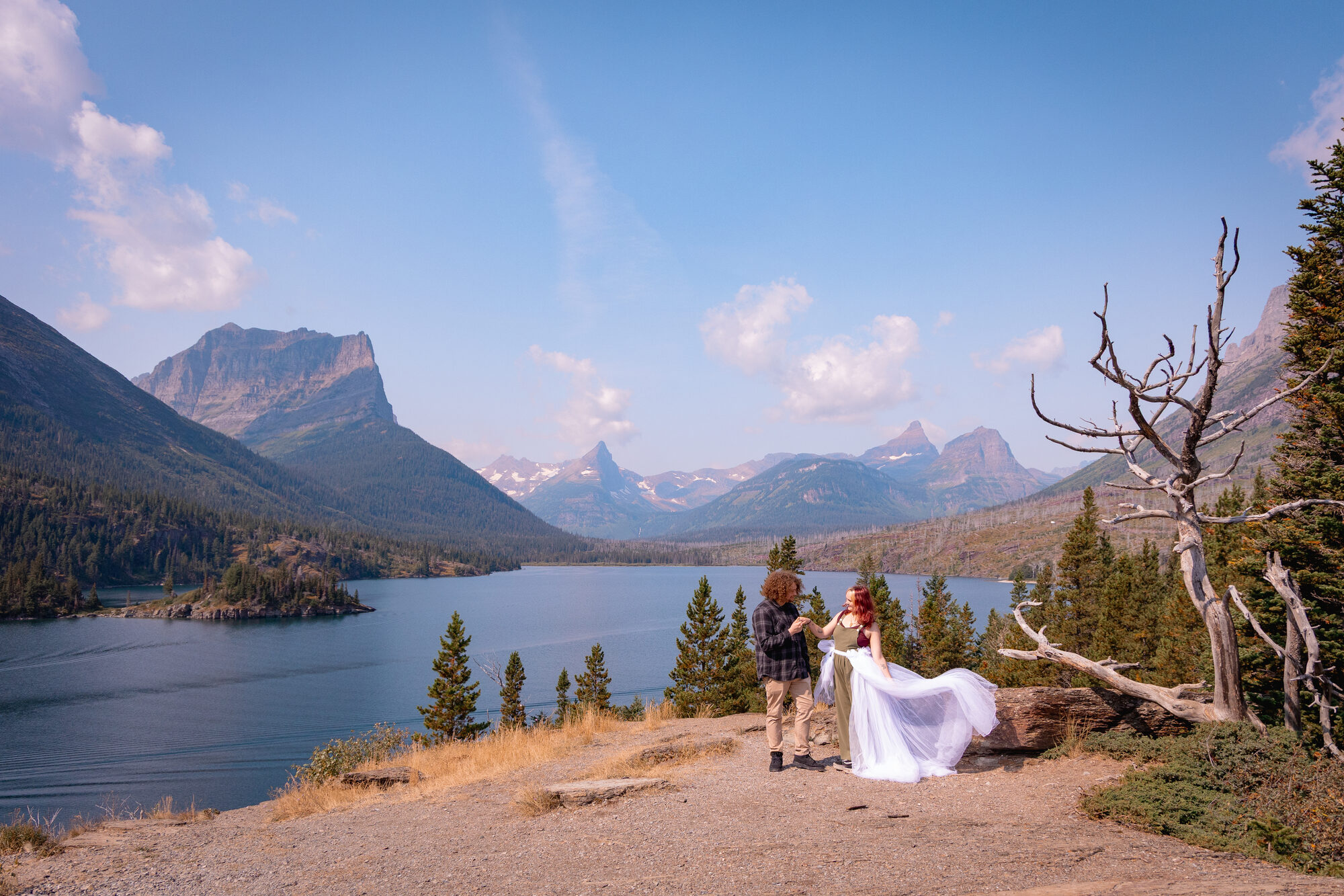 Couple dancing on a rocky outcrop above a turquoise mountain lake, bride's veil catching the wind